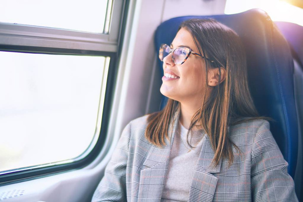 Молодая красивая женщина улыбается счастливой и уверенной. Сидя с улыбкой на лице, путешествуя на поезде
 - Фото, изображение