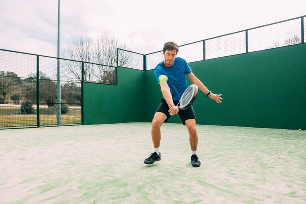 Young man playing paddle tennis on a green court, wearing a blue t-shirt.Sports concept.Copy space - Photo, Image