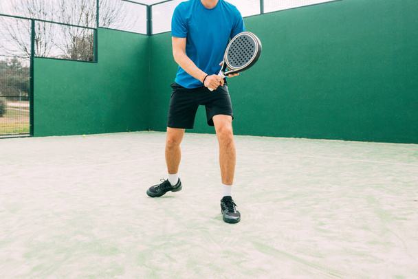 Young man playing paddle tennis on a green court, wearing a blue t-shirt.Sports concept.Copy space - Фото, зображення