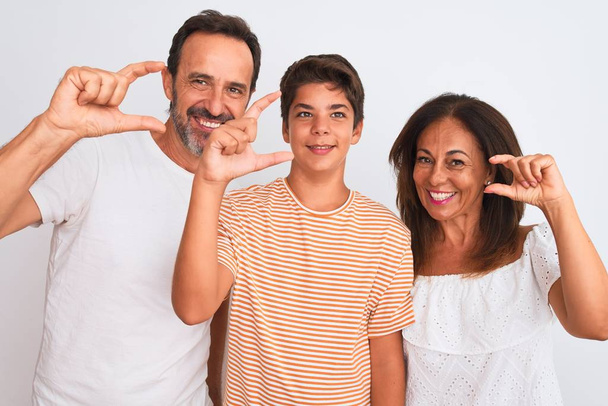 Family of three, mother, father and son standing over white isolated background smiling and confident gesturing with hand doing small size sign with fingers looking and the camera. Measure concept. - Fotoğraf, Görsel