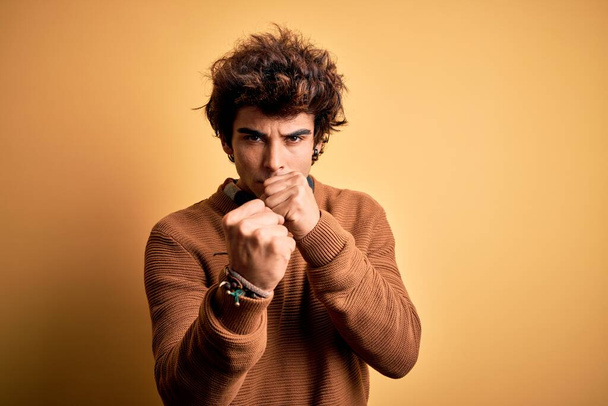 Young handsome man wearing casual shirt and sweater over isolated yellow background Ready to fight with fist defense gesture, angry and upset face, afraid of problem - Foto, Imagen
