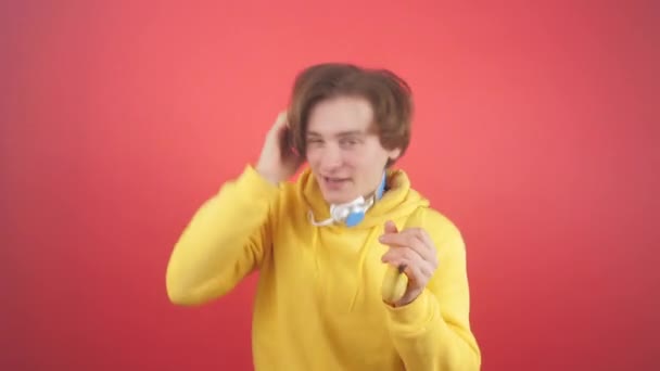 A young man in a sweatshirt sings in a banana on a red background - Materiał filmowy, wideo
