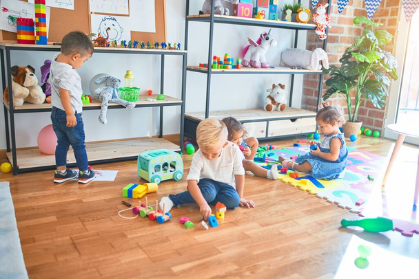 Suloinen ryhmä pikkulapsia leikkimässä paljon leluja päiväkodissa
 - Valokuva, kuva