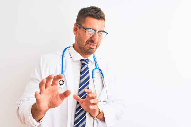 Young handsome doctor man wearing stethoscope over isolated background disgusted expression, displeased and fearful doing disgust face because aversion reaction. With hands raised. Annoying concept. - Photo, image