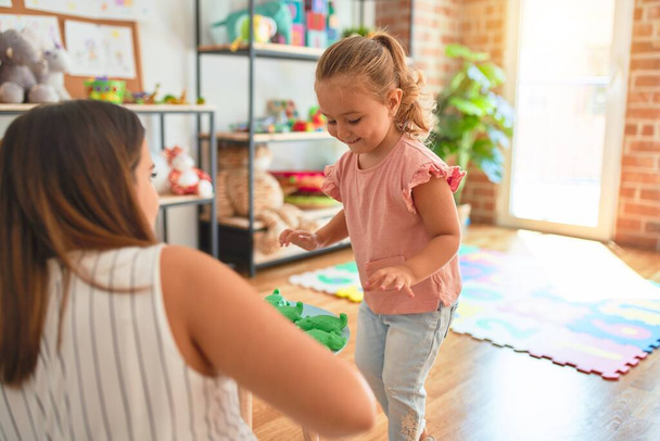 schöne Lehrerin und blonde Studentin Kleinkind Mädchen spielt mit Plastikfröschen Spielzeug im Kindergarten - Foto, Bild