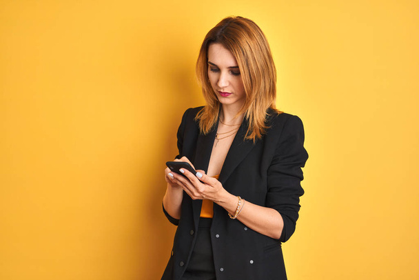 Junge kaukasische elegante Geschäftsfrau mit Smartphone auf isoliertem gelben Hintergrund mit selbstbewusstem Gesichtsausdruck und ernstem Denken - Foto, Bild