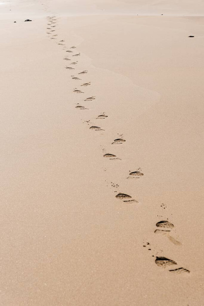 A vertical shot of the footprints of a man on the desert sand on a sunny day - Fotó, kép