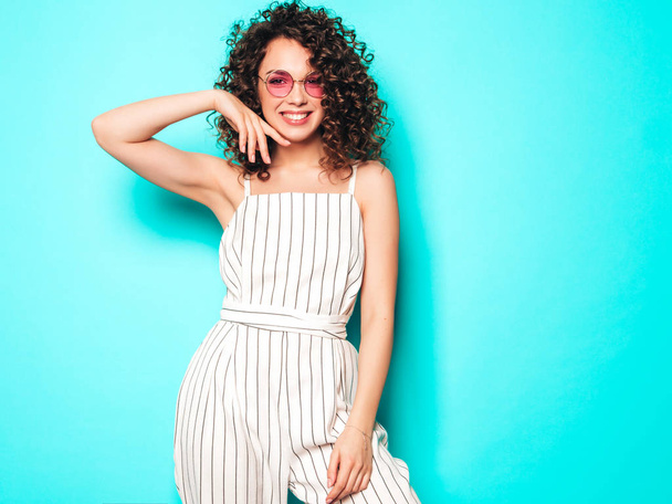 Portrait of beautiful smiling model with afro curls hairstyle dressed in summer hipster clothes.Sexy carefree girl posing in studio near blue wall.Trendy funny and positive woman - Fotografie, Obrázek