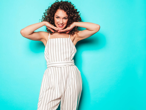 Portrait of beautiful smiling model with afro curls hairstyle dressed in summer hipster clothes.Sexy carefree girl posing in studio near blue wall.Trendy funny and positive woman - Фото, изображение
