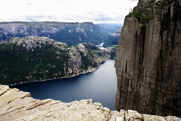 A beautiful scenery of the famous Preikestolen cliffs near a lake under a cloudy sky in Stavanger, Norway - Фото, изображение