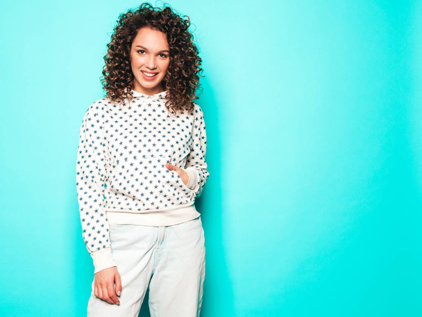 Portrait of beautiful smiling model with afro curls hairstyle dressed in summer hipster clothes.Sexy carefree girl posing in studio near blue wall.Trendy funny and positive woman - Foto, immagini