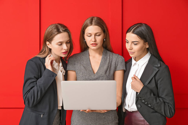 Beautiful young businesswomen with laptop on color background - Photo, Image