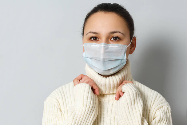 Studio portrait of young woman wearing a face mask, looking at camera, close up, isolated on gray background. Flu epidemic, dust allergy, protection against virus - Фото, зображення