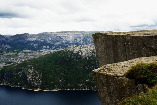 A beautiful scenery of the famous Preikestolen cliffs near a lake under a cloudy sky in Stavanger, Norway - 写真・画像