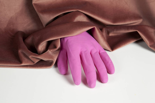 ピンクのベルベットのカーテンから出てきたピンクの膨らんだプラスチック製の家庭用手袋。色の調和。ミニマルな静物カラー写真 - 写真・画像