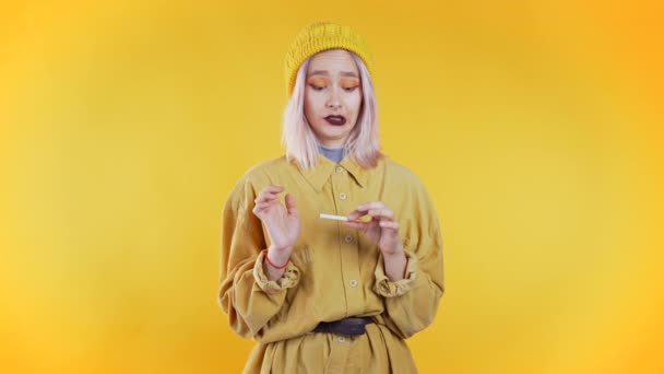 Pretty unusual girl breaking the last cigarette isolated on yellow background. Quit smoking, bad habit concept. - Video, Çekim