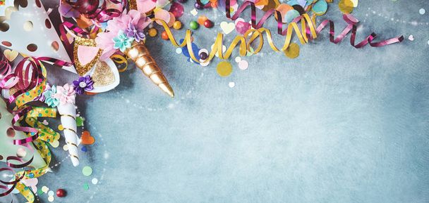 Panorama unicorn banner with festive carnival border of colorful streamers, party hats, candy over a cool blue textured background with copy space - Фото, изображение