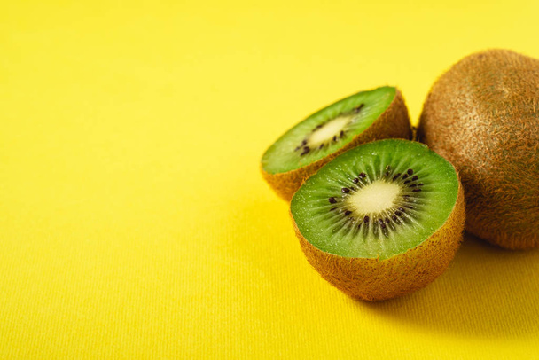 Kiwifrüchte halb in Scheiben geschnitten auf lebendigem, schlichtem, gelbem Hintergrund, Kopierraum, Winkelansicht - Foto, Bild