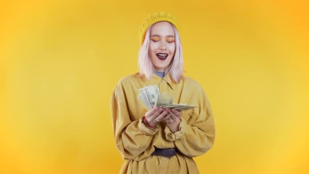 Satisfied happy excited unusual teen girl showing money - U.S. currency dollars banknotes on yellow wall. Symbol of success, gain, victory. - Πλάνα, βίντεο