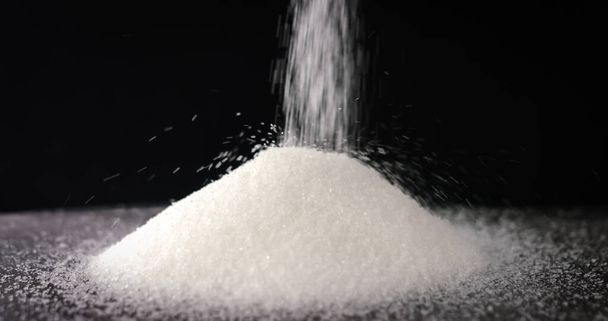 Açúcar caindo em uma mesa no fundo preto
 - Foto, Imagem
