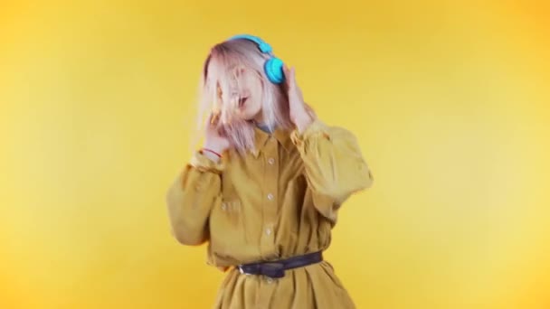 Beautiful woman with pink hair dancing with headphones on yellow studio background. Cute girls portrait. Music, radio, happiness, freedom, youth concept. - 映像、動画