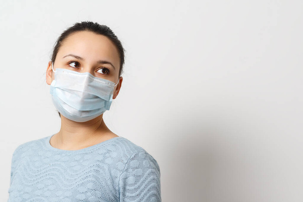 Studio portrait of young woman wearing a face mask, looking at camera, close up, isolated on gray background. Flu epidemic, dust allergy, protection against virus - 写真・画像
