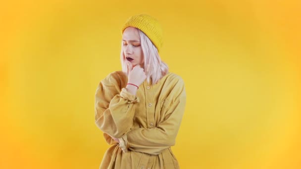 Thinking woman looking up and around on yellow background. Worried contemplative face expressions. Pretty girl model with unusual trendy appearance. - Metraje, vídeo