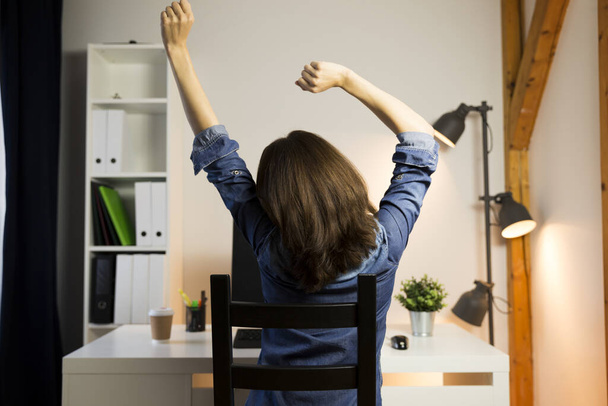 Mulher esticando os braços sentada à mesa no trabalho ao lado do computador. Trabalhando tarde conceito
 - Foto, Imagem