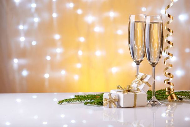 Two glasses with champange, fir tree branch, gift boxes and christmas decorations on a yellow background with lights of garland.  New year and Christmas. - Valokuva, kuva