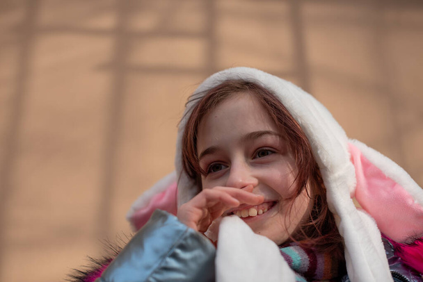 Χαριτωμένο κοριτσάκι με κουκούλα και αυτιά. κορίτσι σε μια οδό λαγουδάκι καπέλο - Φωτογραφία, εικόνα