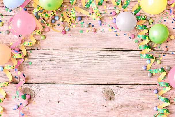 Festival or carnival background in pastel vintage colors on a pink tinged wood background with a frame of streamers, balloons, confetti and candy around copy space - Foto, imagen