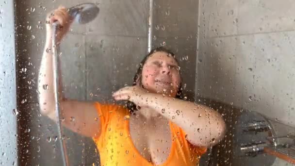 middle-aged woman in an orange T-shirt washes in the shower - Felvétel, videó