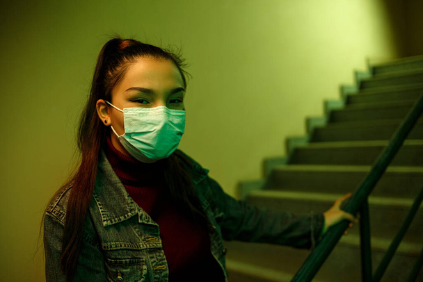 Korunabilir tıbbi maske takan Asyalı bir kızın portresi. Bir hastane ya da binanın merdiven boşluğu. - Fotoğraf, Görsel