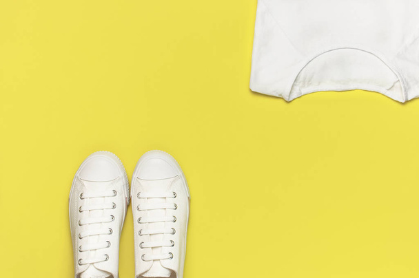 White female fashion sneakers, white T-shirt on yellow orange background. Flat lay top view copy space. Women's shoes. Stylish white sneakers. Fashion blog or magazine concept. Shoe background, sport - 写真・画像