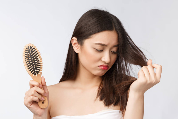 Upset stressed young Asian woman holding damaged dry hair on hands over white isolated background. - Foto, imagen