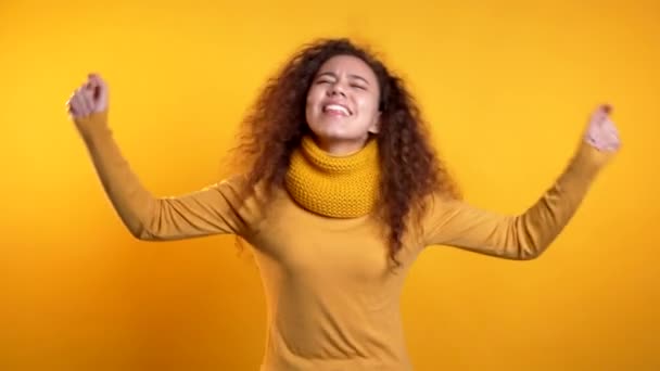 Beautiful woman with curly hair dancing on colorful yellow studio background. Cute girls portrait. Party, happiness, freedom, youth concept. - Video