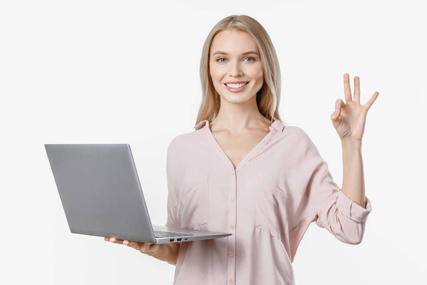 Young blonde girl holding laptop computer and showing ok gesture isolated over white background - Foto, Imagen