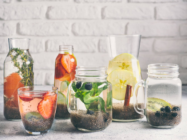 Different chia water in glass on gray background. Chia infused detox water with berries, fruits and herbs. Healthy eating, drinks, diet, detox concept. Copy space for text - Φωτογραφία, εικόνα