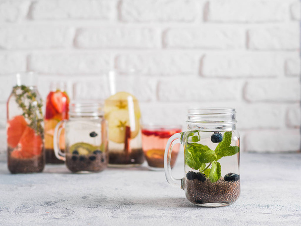 Chia water in mason jar with mint and blueberry on gray cement background. Chia infused detox water with berries, fruits and herbs. Copy space for text. Healthy eating, drinks, diet, detox concept - 写真・画像