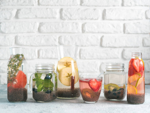 Different chia water in glass on gray background. Chia infused detox water with berries, fruits and herbs. Healthy eating, drinks, diet, detox concept. Copy space for text - Fotó, kép