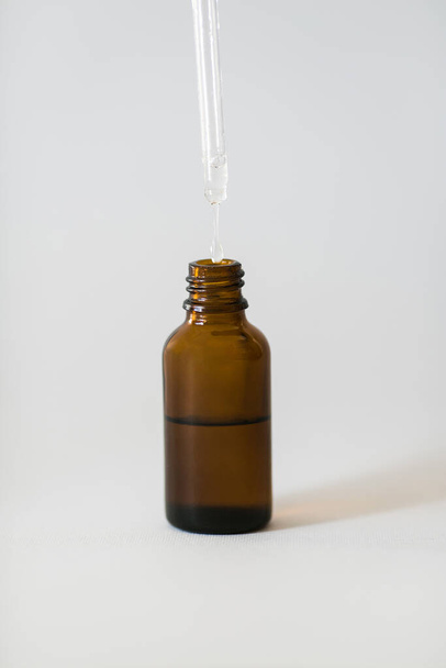 Cosmetic pipette and dark oil bottle with drop closeup on white background. - 写真・画像