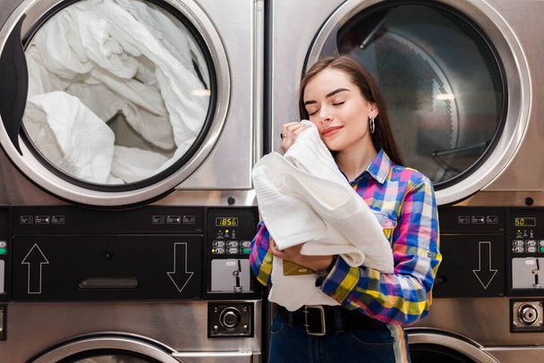 Girl enjoys clean and smelling towels after washing in launderette - Photo, Image