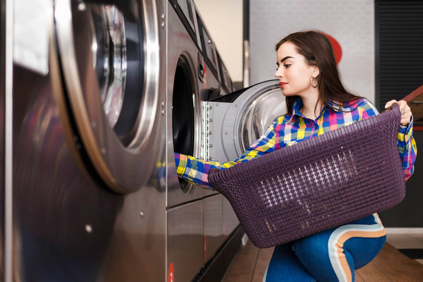 Το κορίτσι βάζει μπουγάδα στο πλυντήριο. γυναίκα σε δημόσια πλυντήρια - Φωτογραφία, εικόνα