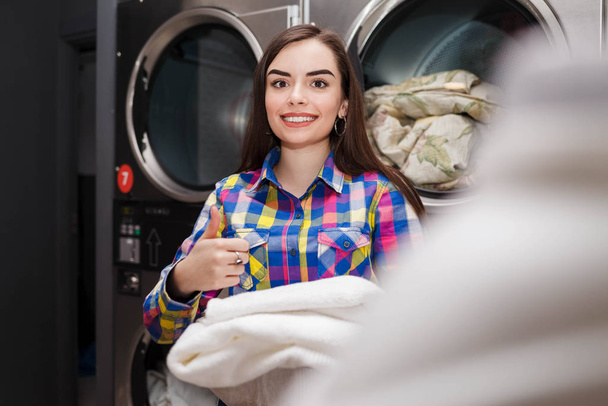 Dziewczyna zadowolona z wyniku prania. Kobieta w pralni pokazuje kciuki do góry - Zdjęcie, obraz