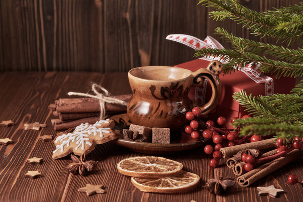 Cup of coffee, gingerbread cookies, gift box, fir tree branches with decorations on a wooden brown background.  Christmas and New Year treat. - Φωτογραφία, εικόνα
