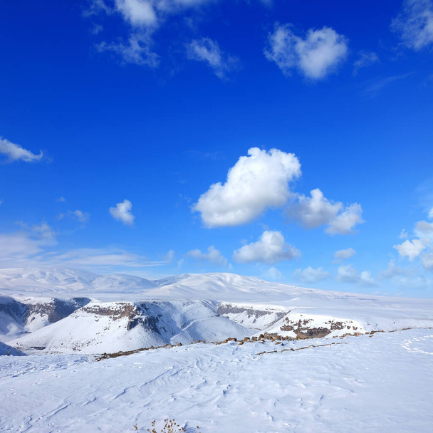 Snow covered empty frozen landscape of mountainside over blue sky with clouds - Foto, Bild