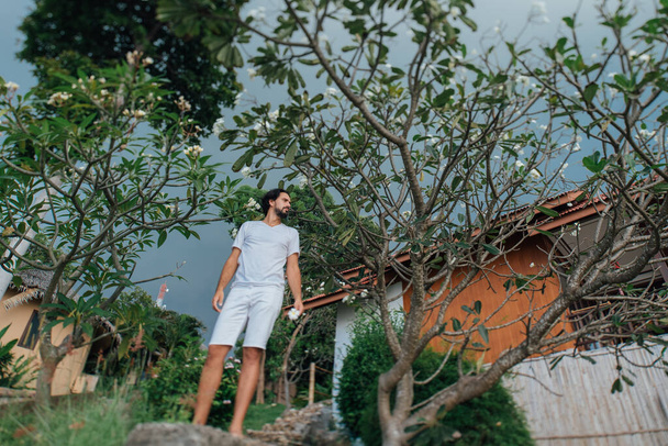 Un hombre vestido de blanco en un jardín tropical
 - Foto, Imagen