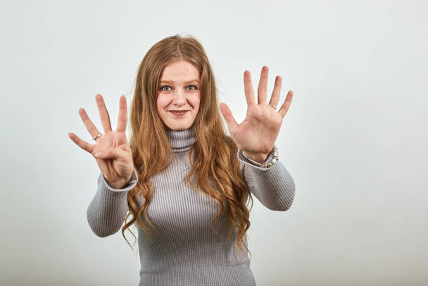 Η γυναίκα με το γκρι πουλόβερ δείχνει το νούμερο 9 με τα δάχτυλά της. - Φωτογραφία, εικόνα
