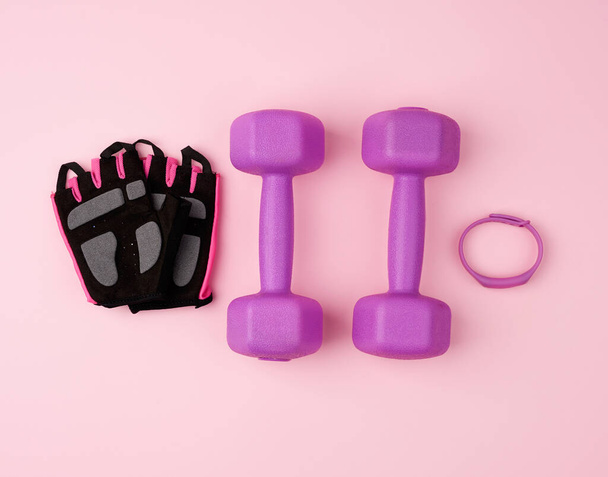 ζεύγος μωβ πλαστικά αλτήρες και μαύρα γάντια σε ροζ πλάτη - Φωτογραφία, εικόνα