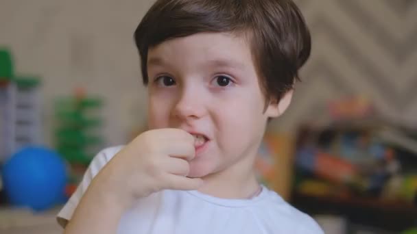 Mały chłopiec stoi w pokoju dziecięcym i potrząsa palcami jak mleczny ząb. Chłopak wyciąga mleczny ząb z ust i jest zaskoczony.. - Materiał filmowy, wideo